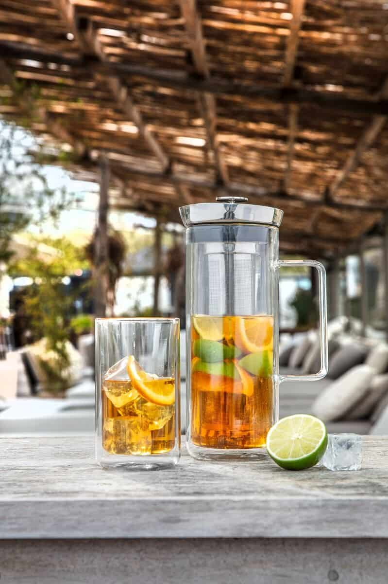Verfrissende zomerlimonade met citrusfruit en ijs in glazen en kan op terras met houten tafel en buitendek, perfect voor ontspannen momenten bij De Heeren van 17.