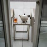 Rustiek theepot en glas met thee op een klein wit terras, uitnodigend en gezellig, perfect voor ontspanning, met focus op comfort en design.