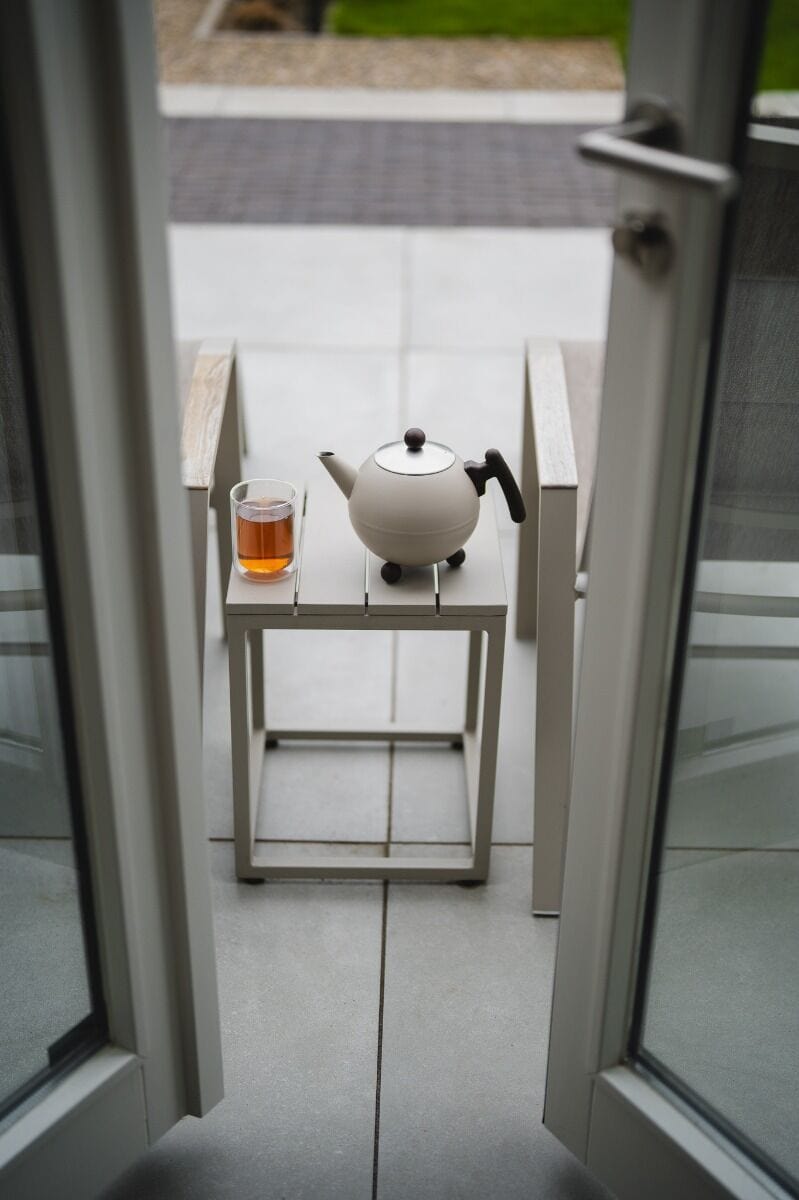 Rustiek theepot en glas met thee op een klein wit terras, uitnodigend en gezellig, perfect voor ontspanning, met focus op comfort en design.