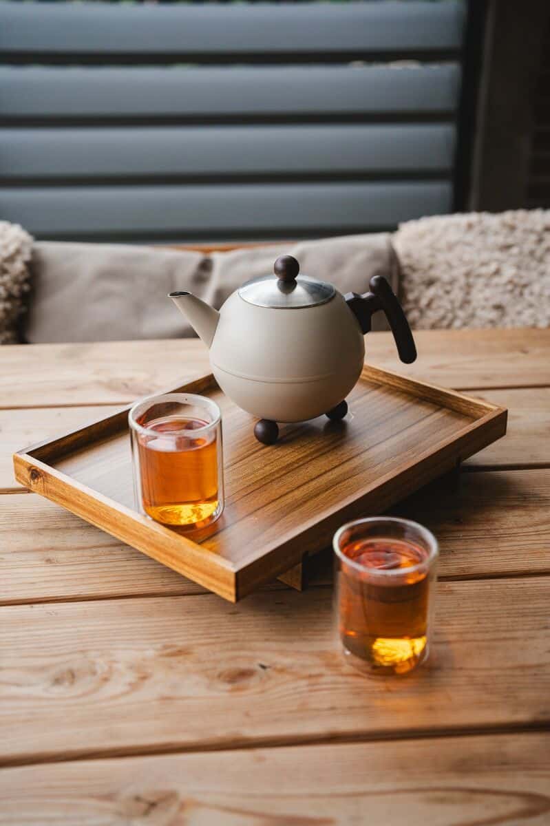 De Heeren van 17 theepot en twee glazen thee op houten dienblad op houten tafel, gezellige sfeer in buitenruimte.