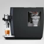 Grote zwarte koffiemachine met doorzichtige zeef en kopje verse espresso eronder, geoptimaliseerd voor koffie & horeca SEO.